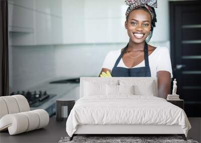 Smiling african american housewife in apron with arms crossed cleaning at home Wall mural